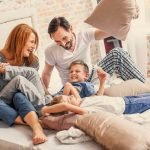 Famiglia felice che gioca insieme sul letto di casa, simbolo di comfort domestico e vita familiare serena.