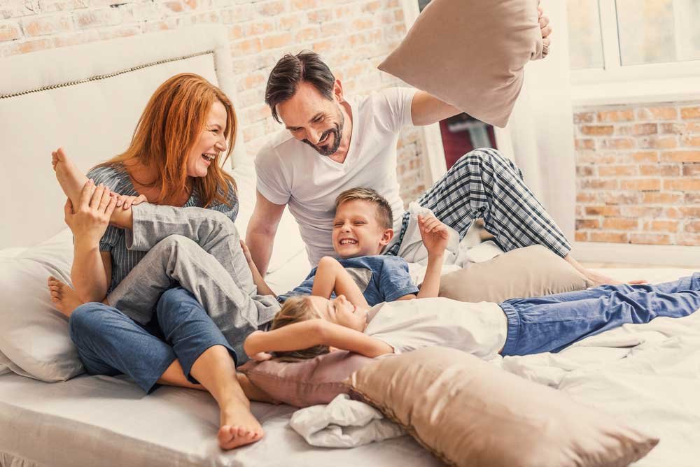 Famiglia felice che gioca insieme sul letto di casa, simbolo di comfort domestico e vita familiare serena.